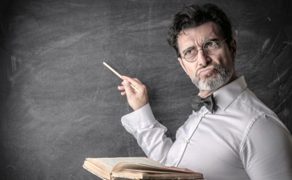 science teacher with a book at a blackboard thinking of answer to question