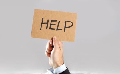 Hand of businessman holding message card asking for help under a pile of papers